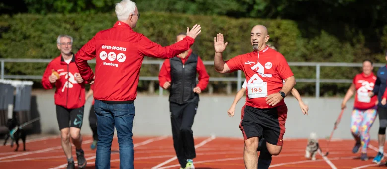 Es sind Läufer auf einer Tartanbahn zu sehen, sie tragen rote Shirts mit Startnummern drauf.
