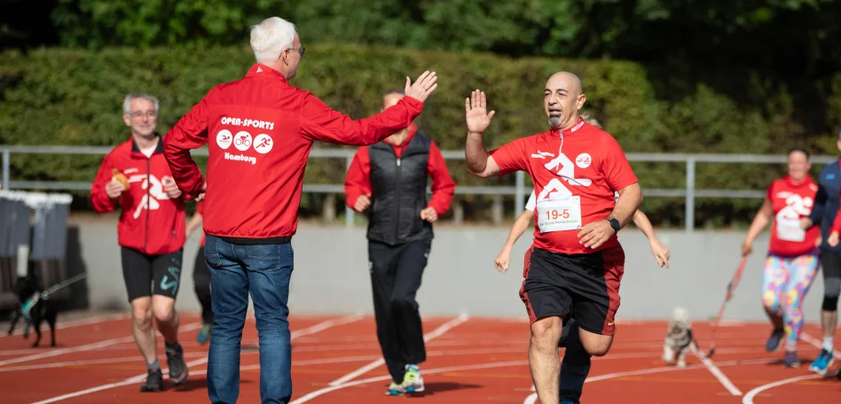Es sind Läufer auf einer Tartanbahn zu sehen, sie tragen rote Shirts mit Startnummern drauf.