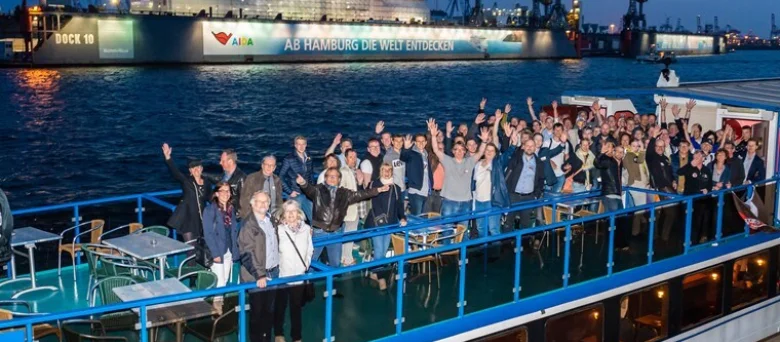 Eine Gruppe von Menschen auf einem Boot, die der Kamera zuwinken.