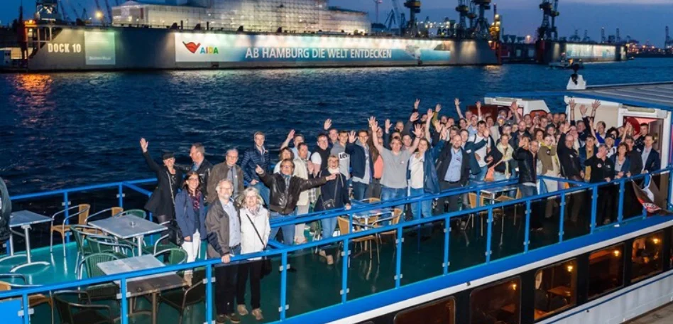 Eine Gruppe von Menschen auf einem Boot, die der Kamera zuwinken.