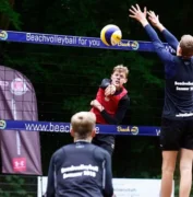 Vier Menschen die gegeneinander Beachvolleyball spielen