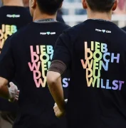 Eine Gruppe von Menschen, mit dem Rücken zur Kamera. Auf ihren T-Shirts steht "Lieb doch wen du willst" in bunter Schrift