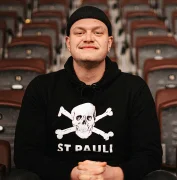 Ein Mann in St. Pauli Pullover und schwarzer Mütze schaut lächelnd in die Kamera