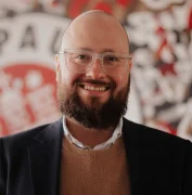 Ein Mann mit Brille und Bart schaut lächelnd in die Kamera