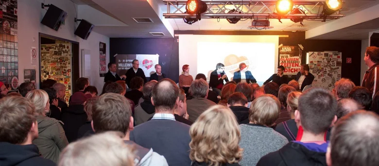 Die FCSP Fanräume von Innen. Viele Menschen stehen vor einer Bühne, während jemand eine Rede hält
