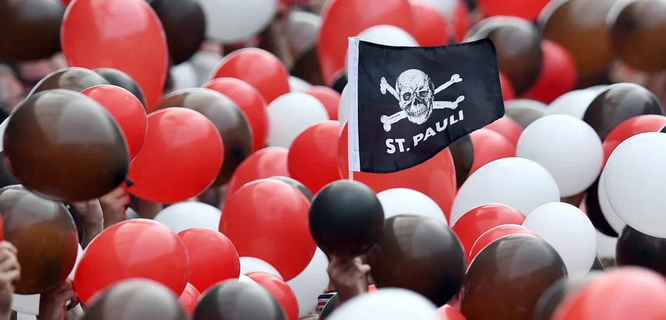 Eine Menschenmenge die Ballons in rot, braun und weiß hochhält. Mittendrin eine kleine St. Pauli Flagge mit Totenkopf
