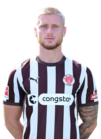 Louis Oppie, Fußballspieler des FC St. Pauli, steht mit verschränkten Armen vor der Kamera. Er trägt das braun-weiß gestreifte Heimtrikot des Vereins mit dem Vereinslogo auf der Brust und einem ASTRA-Logo auf dem Ärmel. Auffällig sind seine blond gefärbten Haare und die Tätowierung auf seinem rechten Arm.