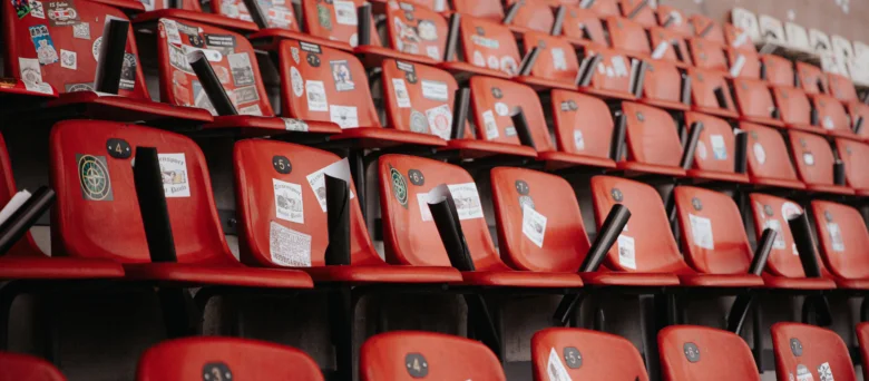 Man sieht einen leeren Teil des Stadions. Die sitze sind rot und mit Stickern beklebt.