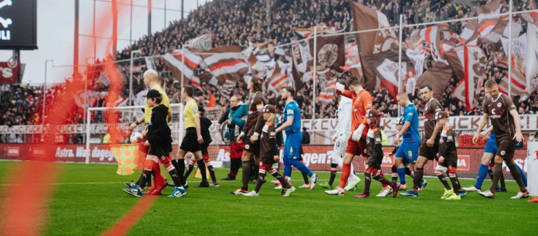Mannschaft läuft mit den Einlaufkindern ein. Man sieht rote Luftschlangen durch's Bild fliegen.