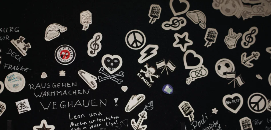 Man sieht eine Wand im Stadion voller Sticket. Neben den Stickern steht handschriftlich geschrieben: "Raus gehen. Warmmachen. Weghauen!"