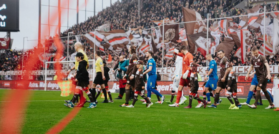 Mannschaft läuft mit den Einlaufkindern ein. Man sieht rote Luftschlangen durch's Bild fliegen.