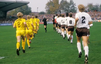Die Mannschaften des FC St. Pauli und Borussia Dortmund laufen auf den Rasen des Millerntor-Stadions, alle Spieler sind von hinten zu sehen.