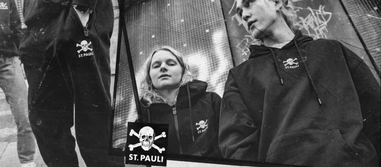 Man sieht eine Frau und einen Mann mit einem St. Pauli-Hoodie. In der Bildcollage ist zusätzlich eine St. Pauli-Hose zu sehen.
