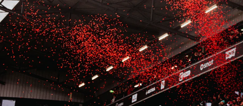 Man sieht eine Tribüne im Stadion. Es regnet rotes Konfetti.