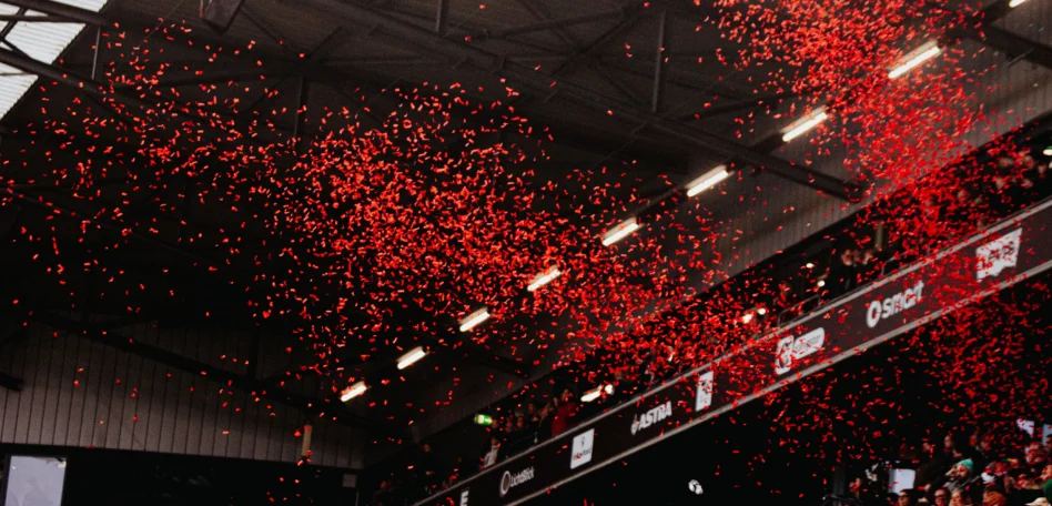 Man sieht eine Tribüne im Stadion. Es regnet rotes Konfetti.